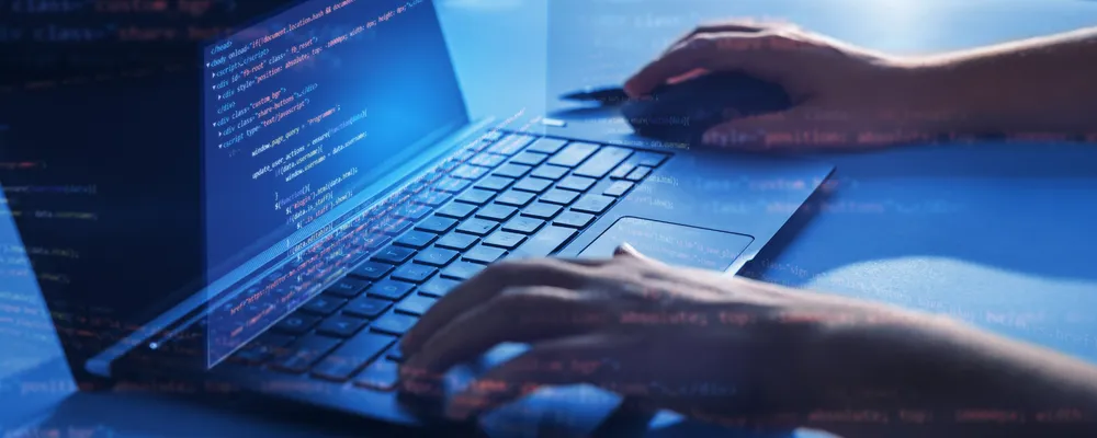 Hands typing on a computer, with 3D code floating around it.